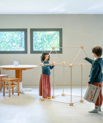 Children building a a tent structure using the Trigonos wooden kernel organic construction set in a dining room setting