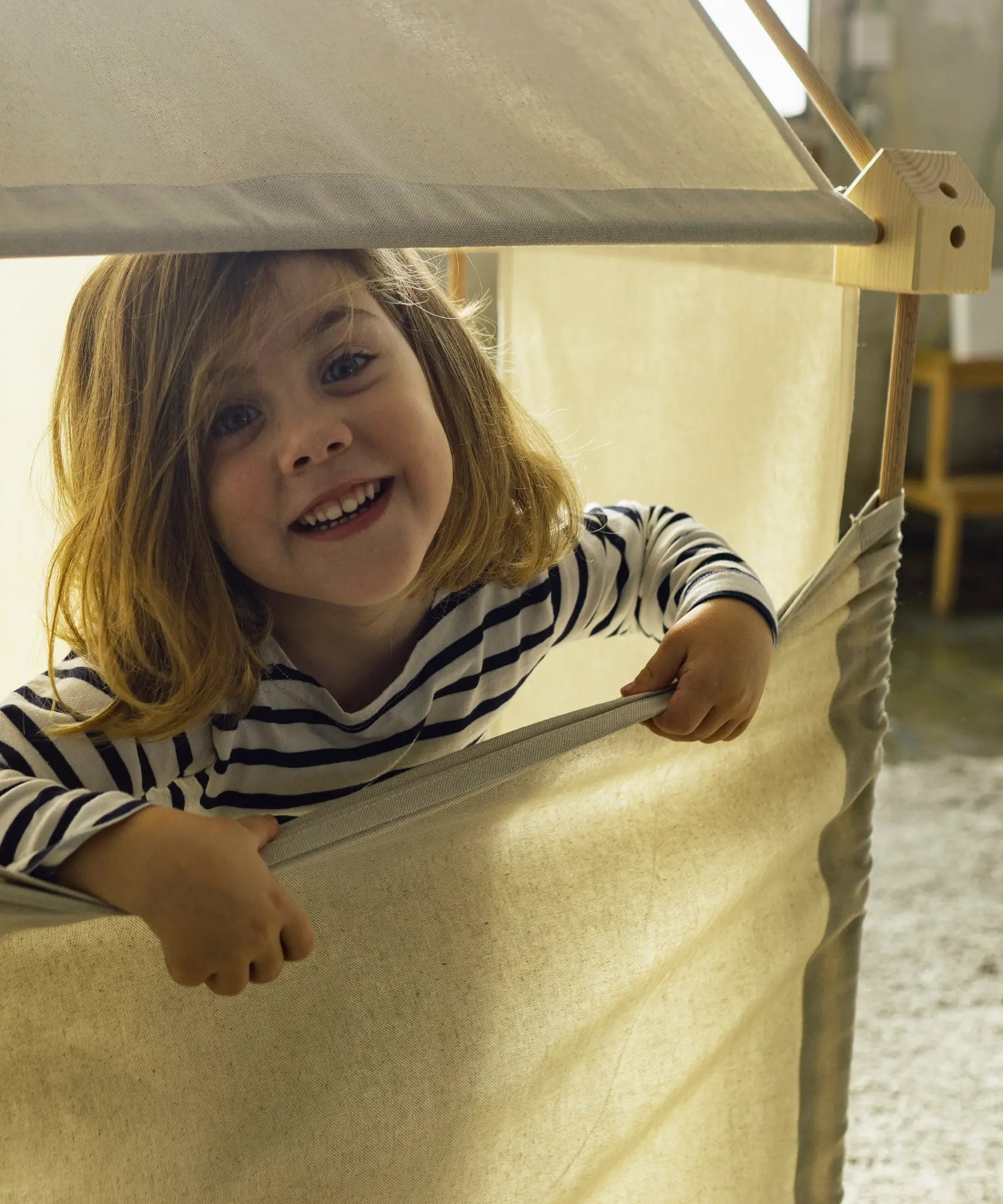 Child pulling a white cotton sheet down from the wooden frame made from the Trigonos kernel organic set