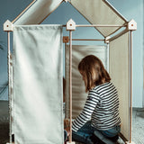 Child sitting inside a tent structure made from the Trigonos wooden kernel organic construction set with white cotton sheets on the roof and sides