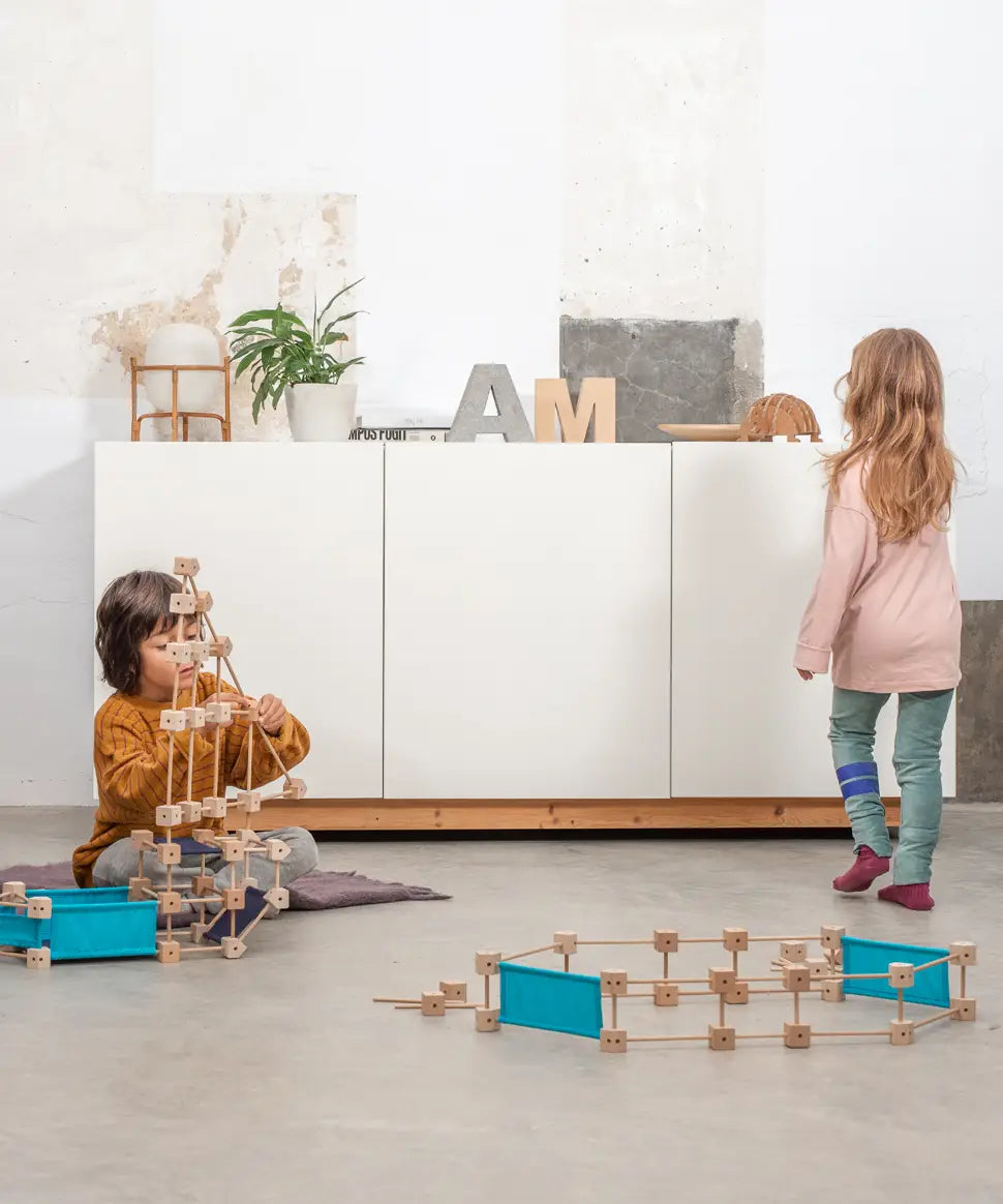 Children playing with different pieces from the Trigonos wooden medium construction kit on a concrete floor