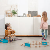Children playing with different pieces from the Trigonos wooden medium construction kit on a concrete floor