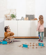 Children playing with different pieces from the Trigonos wooden medium construction kit on a concrete floor