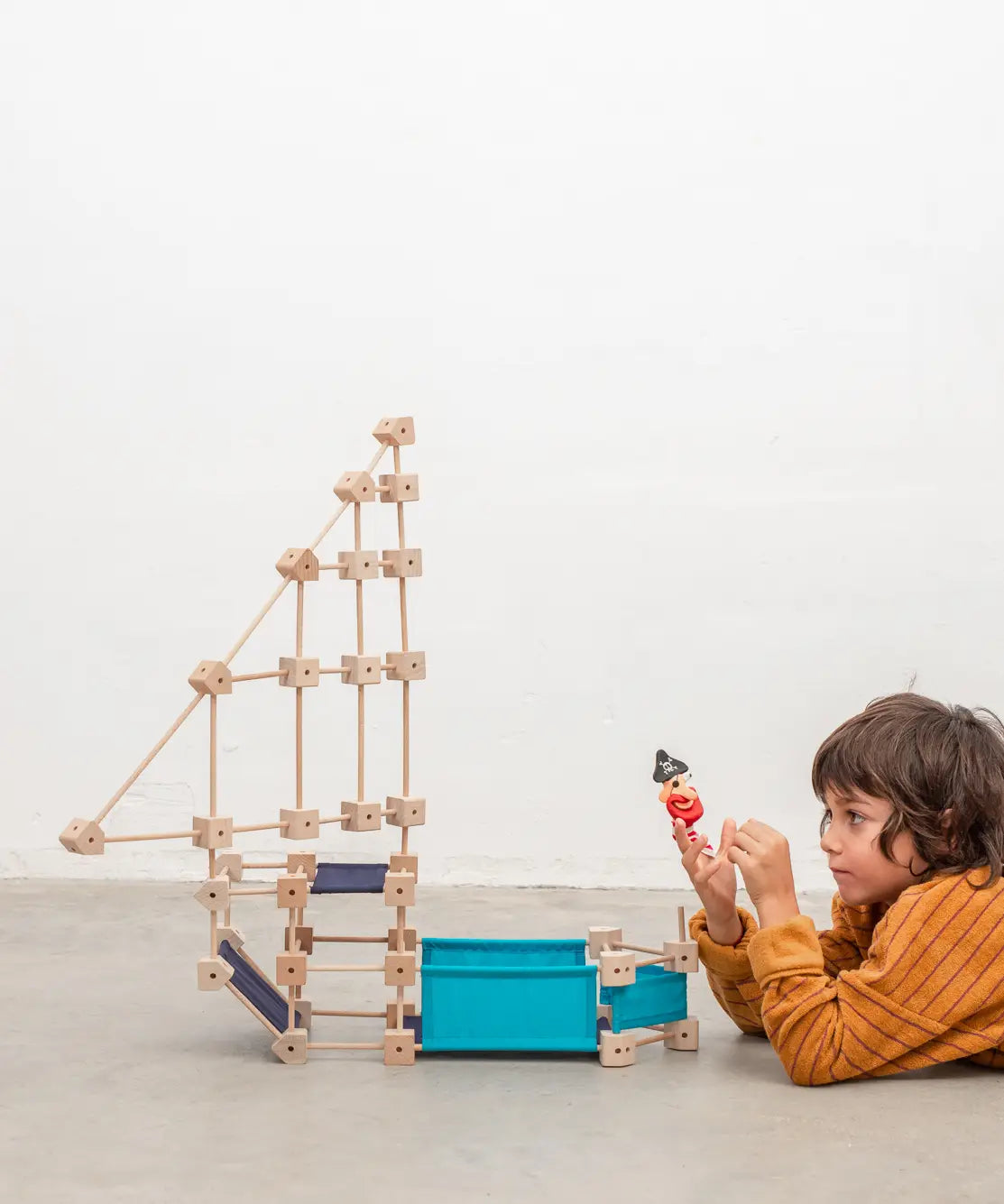 A pirate ship made from the Trigonos wooden medium construction kit standing next to a child on a concrete floor