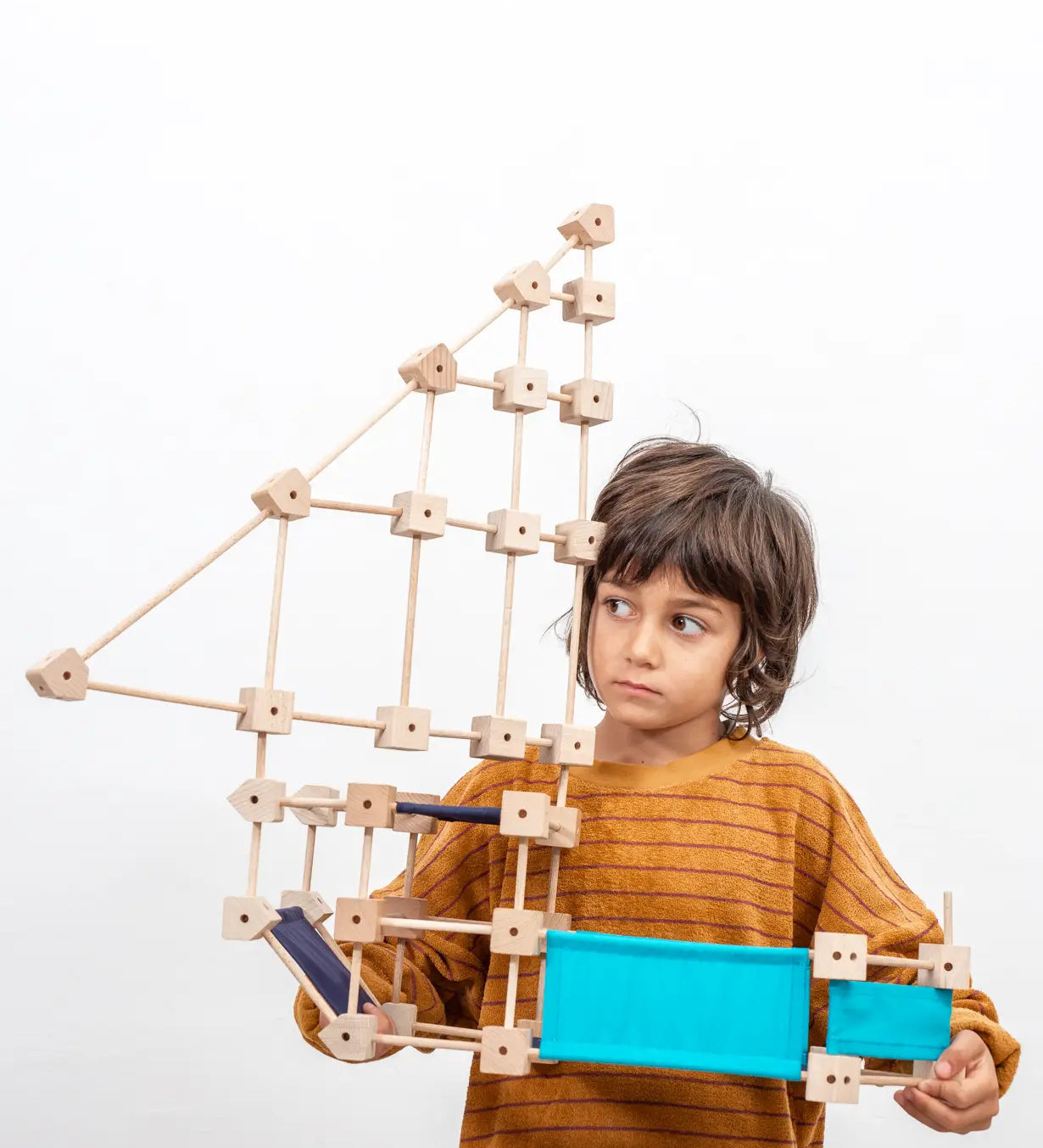 Child holding a pirate ship made from the Trigonos medium construction kit showing dark and blue cotton sheets 