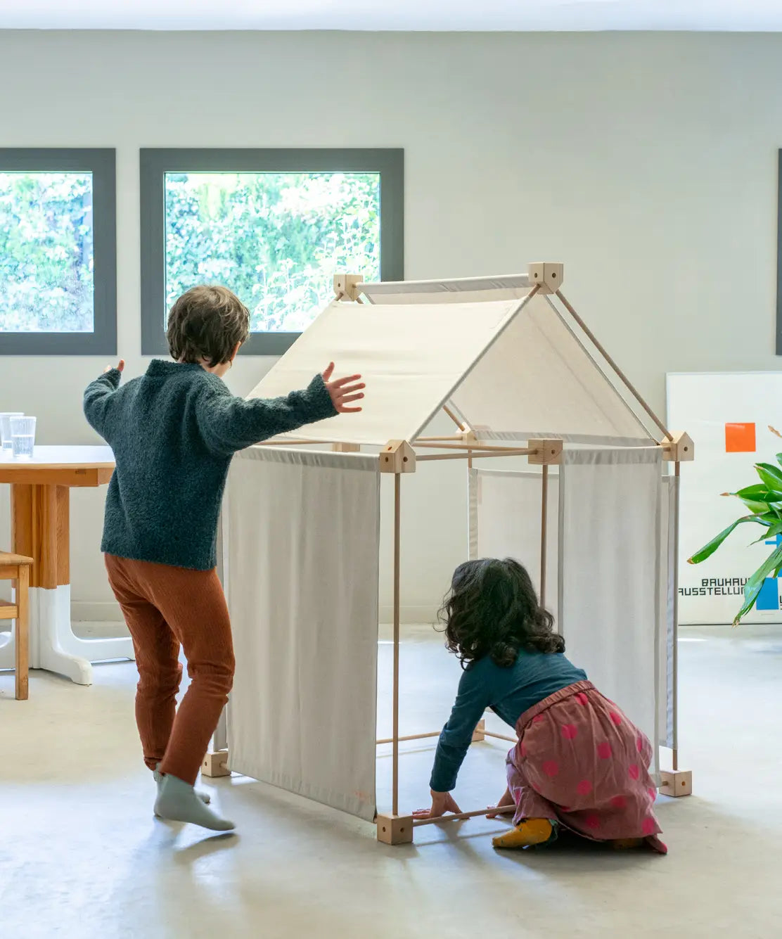 Children building a tent using the Trigonos kernel organic set showing white cotton sheets on the sides and roof