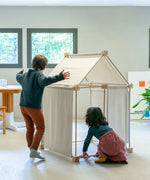 Children building a tent using the Trigonos kernel organic set showing white cotton sheets on the sides and roof