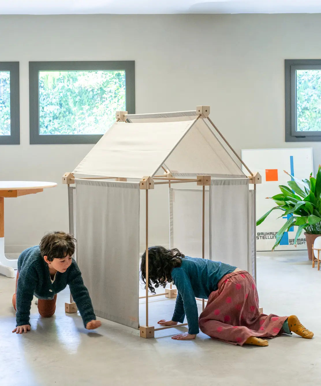 Children playing inside a tent made from the Trigonos wooden kernel organic construction set on a concrete surface