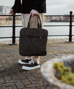 A woman standing next to a city canal, holding the Turtle Bags zig zag duffle bag