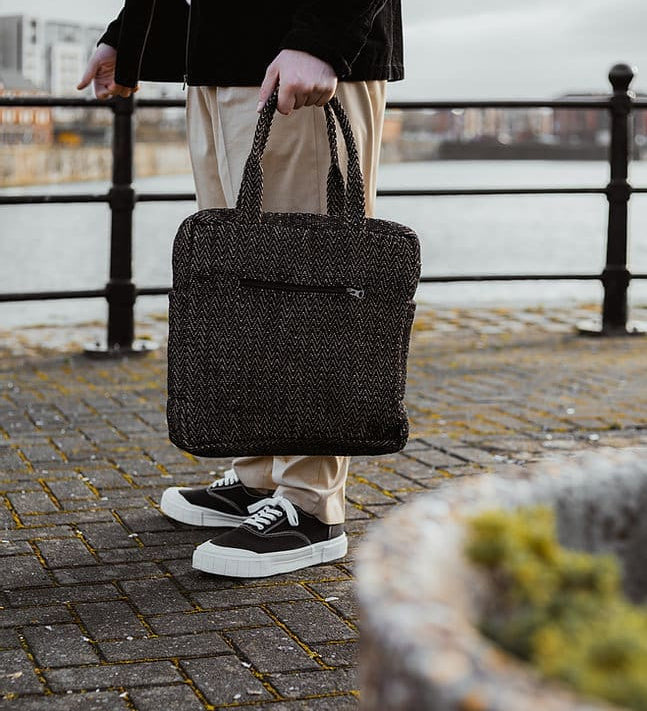 A woman standing next to a city canal, holding the Turtle Bags zig zag duffle bag