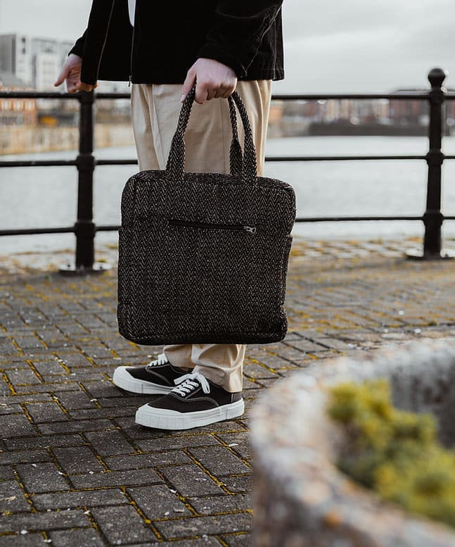 A woman standing next to a city canal, holding the Turtle Bags zig zag duffle bag
