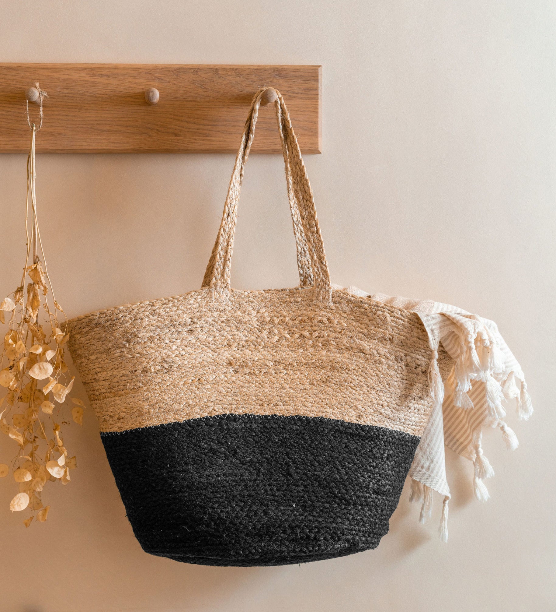 The Turtle Bags hand woven and fair trade jute basket bag with handles, and a black colour block design, hanging on a peg