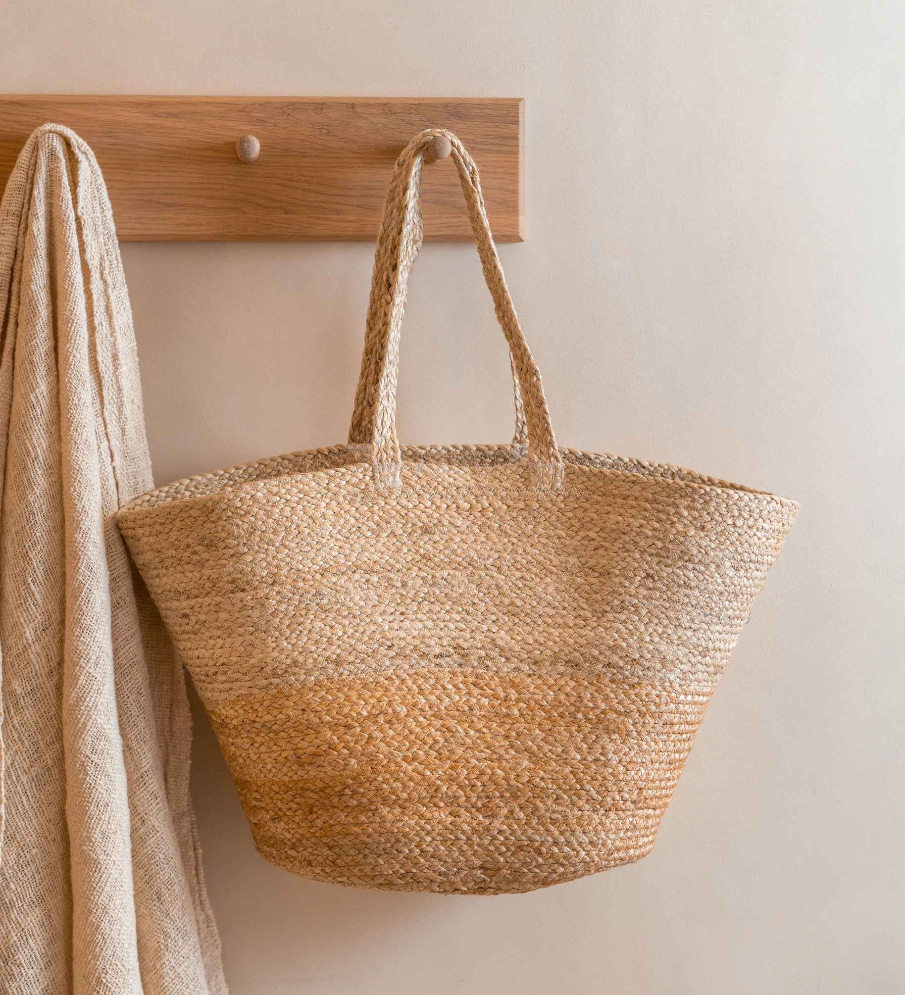 The Turtle Bags hand woven and fair trade jute basket bag with handles, and a natural colour block design, hanging on a peg