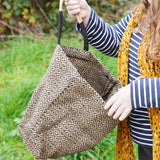 A woman opening The Turtle Bags hand woven fair trade jute tote bag in a diamond pattern design