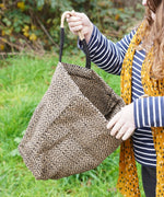 A woman opening The Turtle Bags hand woven fair trade jute tote bag in a diamond pattern design