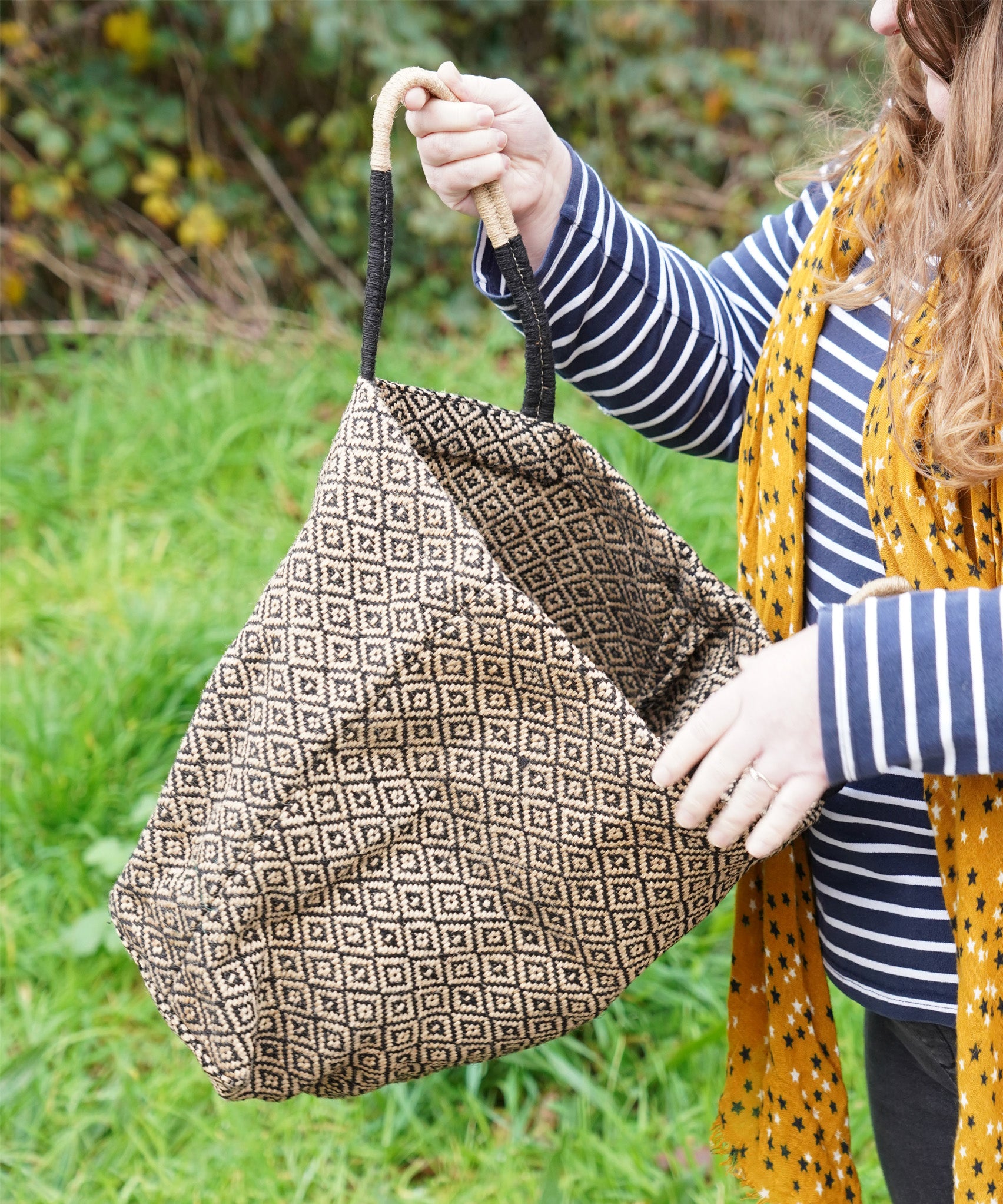 A woman opening The Turtle Bags hand woven fair trade jute tote bag in a diamond pattern design