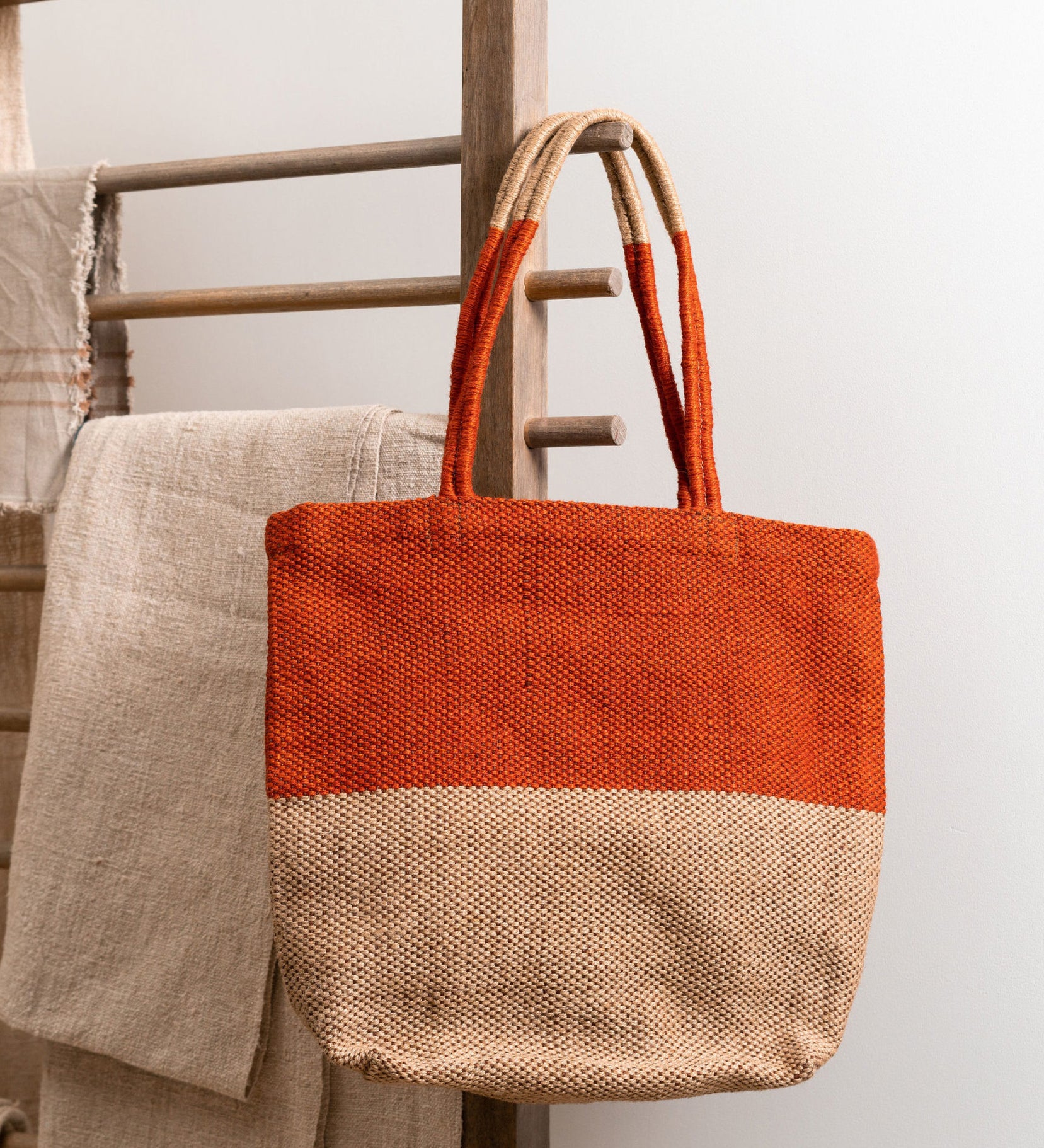 The Turtle Bags hand woven fair trade jute tote bag in an orange paprika colour block design, hanging on a wooden drying rack