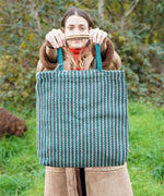 A woman holding up the Turtle Bags hand woven jute tote bag, in a teal stripe design with medium length handles