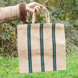 A hand holding out The Turtle Bags hand woven jute tote bag in a green and black stripe design