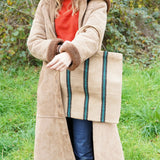 A woman carrying a Turtle Bags hand woven jute stripe bag with short handles, in a green and black stripe
