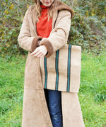 A woman carrying a Turtle Bags hand woven jute stripe bag with short handles, in a green and black stripe