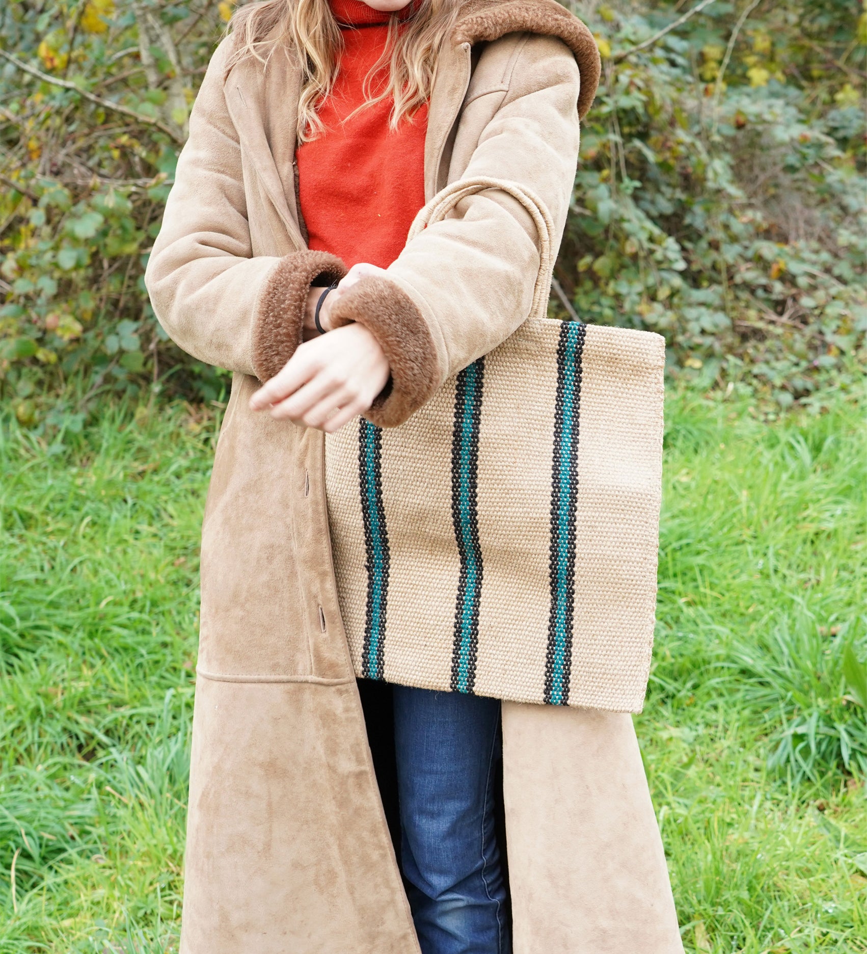 A woman carrying a Turtle Bags hand woven jute stripe bag with short handles, in a green and black stripe