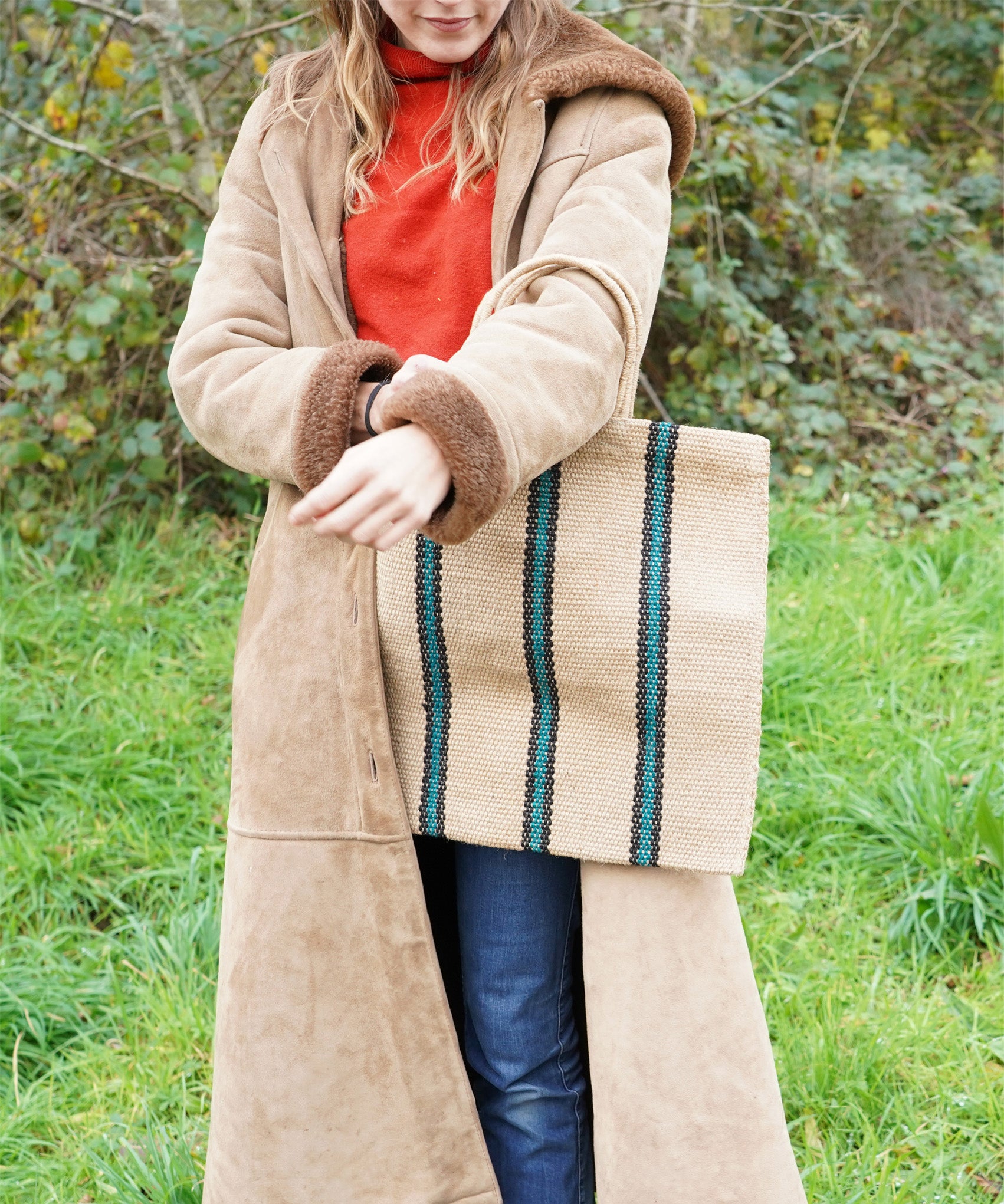 A woman carrying a Turtle Bags hand woven jute stripe bag with short handles, in a green and black stripe