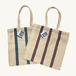 Two Turtle Bags hand woven jute tote bags with long handles, one in a green and black stripe design and one with red and black stripes