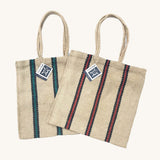 Two Turtle Bags hand woven jute tote bags with long handles, one in a green and black stripe design and one with red and black stripes