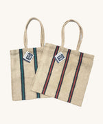Two Turtle Bags hand woven jute tote bags with long handles, one in a green and black stripe design and one with red and black stripes