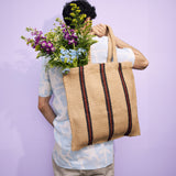 The back of a man carrying a Turtle Bags hand woven jute shopper tote bag in a red stripe design over his shoulder, with a bouquet of flowers inside
