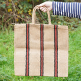 A hand holding The Turtle Bags hand woven jute tote bag with short handles in a red and black stripe design