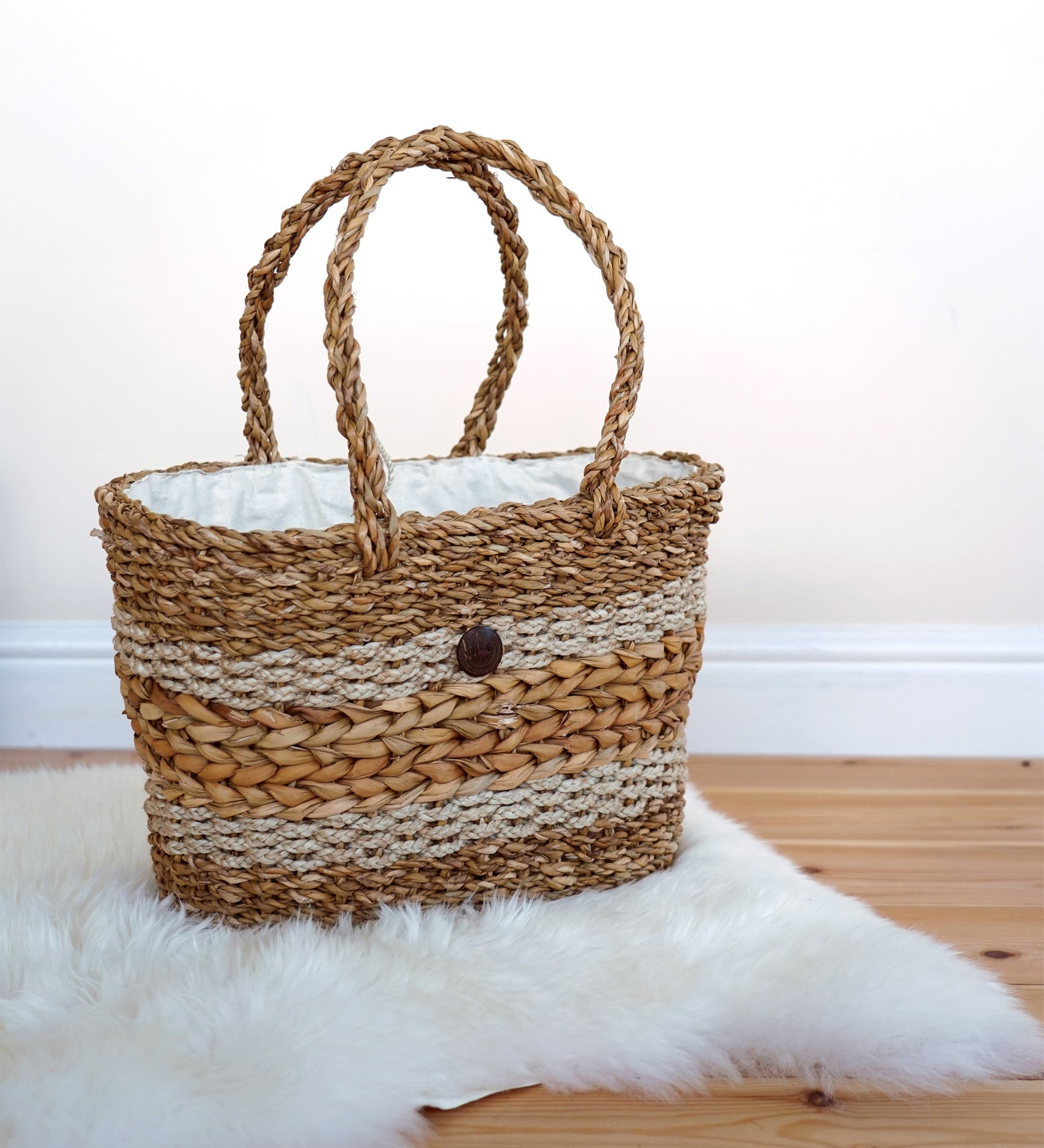 The Turtle Bags hand woven fair trade seagrass basket with handle, positioned on a furry white rug