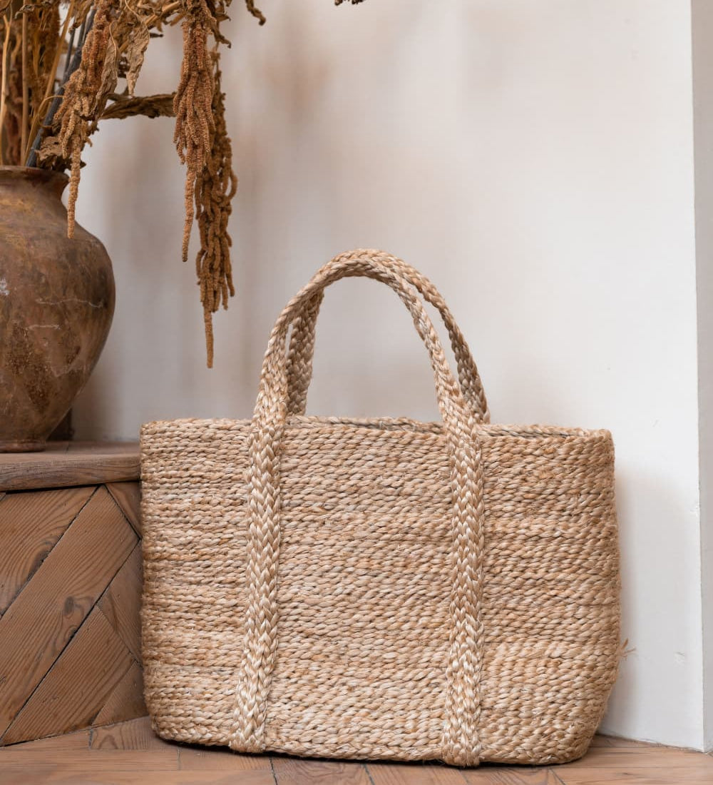 The Turtle bags Fair Trade and hand woven jute basket with handles, stood upright on a wooden floor