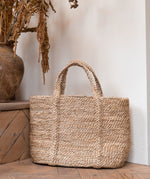 The Turtle bags Fair Trade and hand woven jute basket with handles, stood upright on a wooden floor