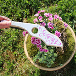 Person holding the Vah Arabella Unicorn Wooden Crossbow showing the design on the side with grass and flowers in the background