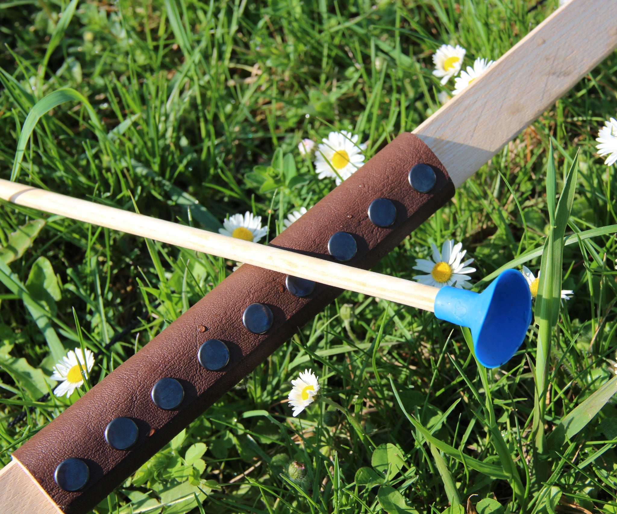 A close up of the brown coloured leather look grip on the Vah Junior Wooden Bow. A blue tipped arrow can be seen alongside it. 