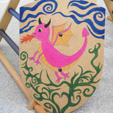 A VAH DIY shield hand painted with a pink dragon. The Shield has been placed resting on the side of a Trimblimb climbing frame. 