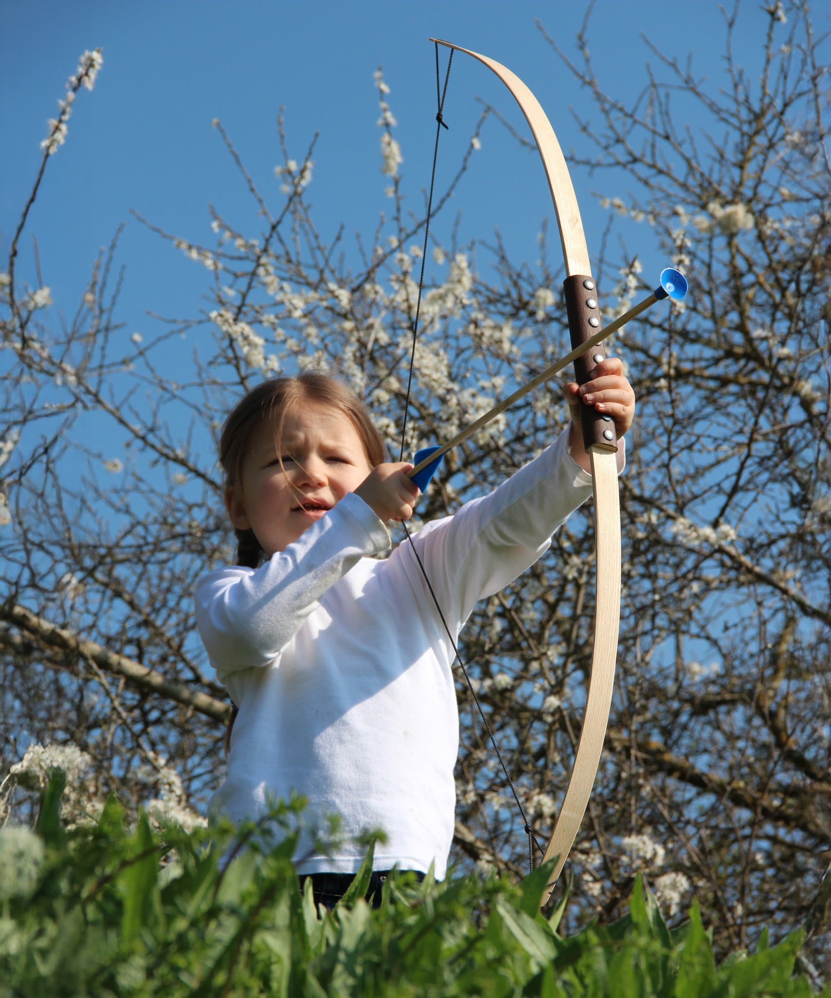 A child holding up the Vah Junior Wooden Bow with a blue Safety Arrow in placed ready to be fired. 