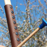 A close up of the brown coloured leather look grip on the Vah Junior Wooden Bow. A blue tipped arrow can be seen alongside it. 