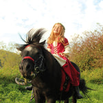 Child wearing the Vah Red Little Marian costume Dress with a cream coloured floral crown whilst riding a pony