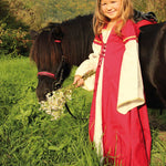 Child wearing the Vah Red Little Marian costume Dress with a matching headpiece holding a bunch of wild daisies. The child is standing next to a pony