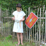 Child wearing the Vah Spartacus Roman Tunic with the red roman alexius shield placed on a fence next to them