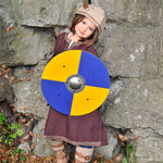 A child wearing the Vah Viking Tunic costume with a Viking helmet holding up a round toy shield.
