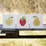 Vah Wooden Fruit Target Trio for Safety Arrows. One target has a apple, one has a strawberry and the third has a pear. They can be seen placed all lined up next to each other on a wooden surface. 