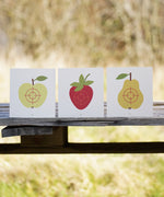 Vah Wooden Fruit Target Trio for Safety Arrows. One target has a apple, one has a strawberry and the third has a pear. They can be seen placed all lined up next to each other on a wooden surface. 