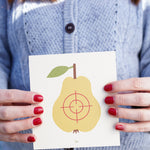 A close up of an an adult's hand holding onto the pear Vah Wooden Fruit Target.