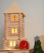 A close up of a tower built using pieces from the Walachia Vario XL Building Set 184 Pieces. Fairy lights have been placed inside the construct ion, a Babipur elephant figure has been placed besides it. This modular wooden building block system is perfect for those who enjoy a challenge. The sets are available in various sizes at Babipur. 