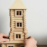 An adult's hand straightening a tower built using pieces from the Walachia Vario XL Building Set 184 Pieces.  This modular wooden building block system is perfect for those who enjoy a challenge. The sets are available in various sizes at Babipur.  