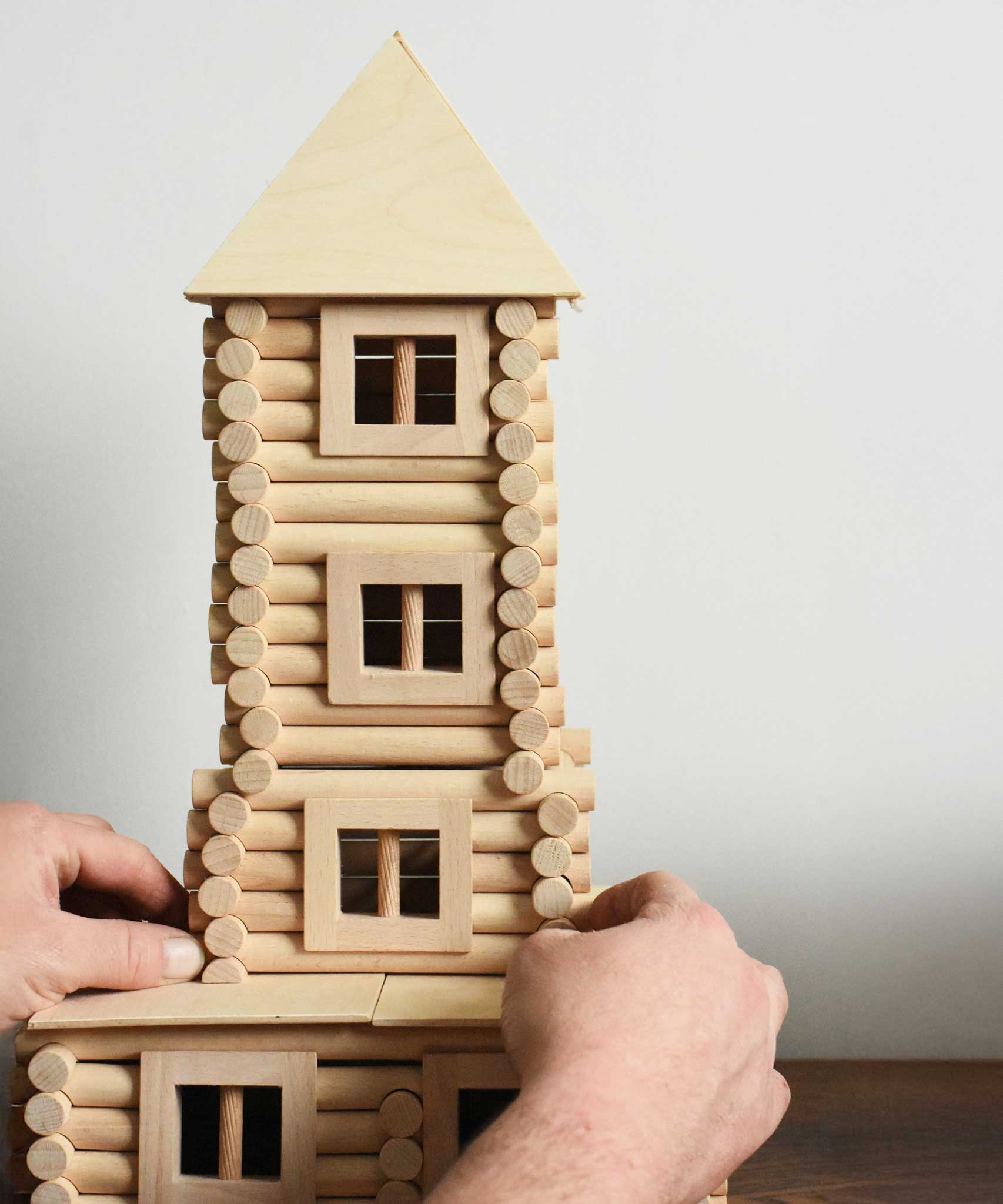 An adult's hand straightening a tower built using pieces from the Walachia Vario XL Building Set 184 Pieces.  This modular wooden building block system is perfect for those who enjoy a challenge. The sets are available in various sizes at Babipur.  