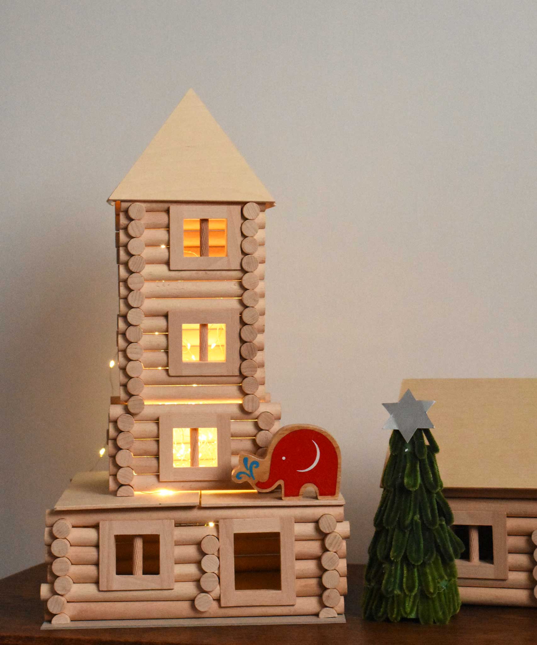 A tower built using pieces from the Walachia Vario XL Building Set 184 Pieces. There is a wooden Lanka Kade Babipur elephant figure placed on the tower with a handmade Christmas tree craft next to it.   This modular wooden building block system is perfect for those who enjoy a challenge. The sets are available in various sizes at Babipur.  